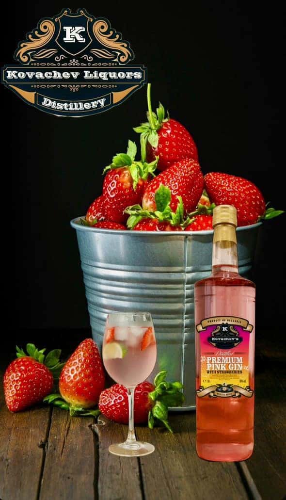 Fresh strawberries and pink gin bottle with berry-themed cocktail on a rustic wooden table.